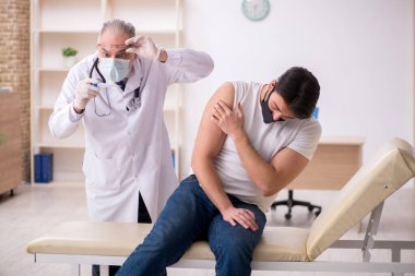 Genç erkek hasta aşı konseptinde yaşlı doktoru ziyaret ediyor.