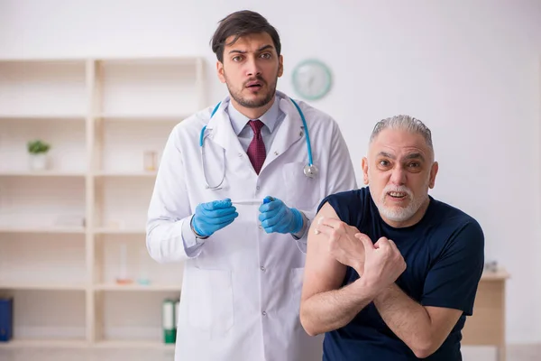 Oude mannelijke patiënt op bezoek bij jonge mannelijke arts in vaccinatiecentrum — Stockfoto