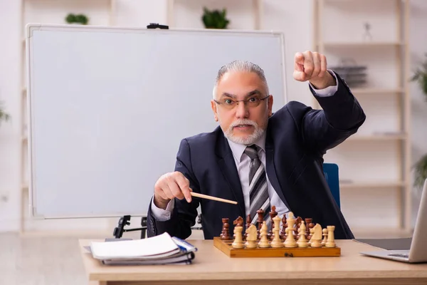 Starý muž zaměstnanec hraje šachy na pracovišti — Stock fotografie