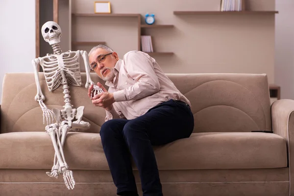 Старик сидит на диване с женским скелетом — стоковое фото
