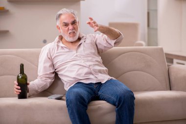 Yaşlı adam evde alkol içiyor.
