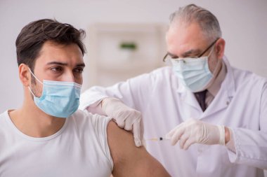 Genç erkek hasta yaşlı erkek doktoru aşıyla ziyaret ediyor.