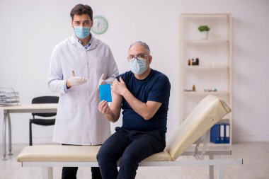 Yaşlı bir erkek hasta aşıyla genç bir doktoru ziyaret ediyor.