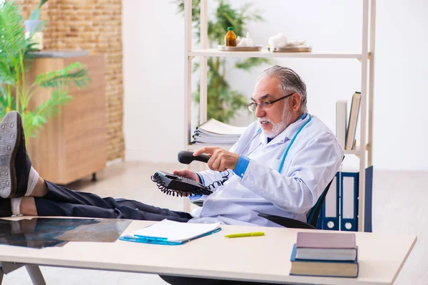 Dokter pria tua berbicara melalui telepon di klinik — Stok Foto