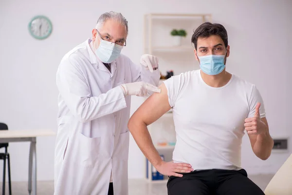 Mladý mužský pacient na návštěvě starého mužského lékaře ve vakcinaci conce — Stock fotografie