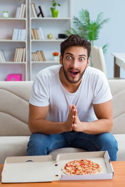 Pizza yiyen adam evde yemek yiyor, dinleniyor.