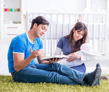 Yeni doğmuş bebekleriyle halıda oturan genç ebeveynler.