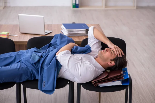 Ung manlig anställd sover på kontoret på stolar — Stockfoto