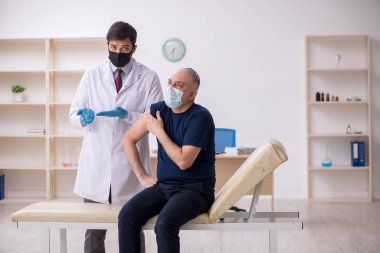 Yaşlı bir erkek hasta aşıyla genç bir doktoru ziyaret ediyor.