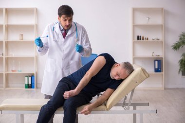 Yaşlı bir erkek hasta aşıyla genç bir doktoru ziyaret ediyor.