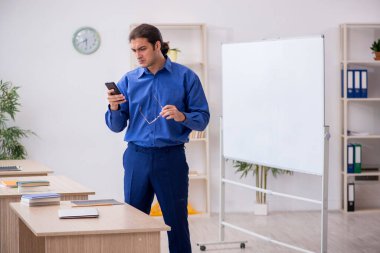 Genç erkek öğretmen ders sırasında elinde akıllı telefon tutuyor.