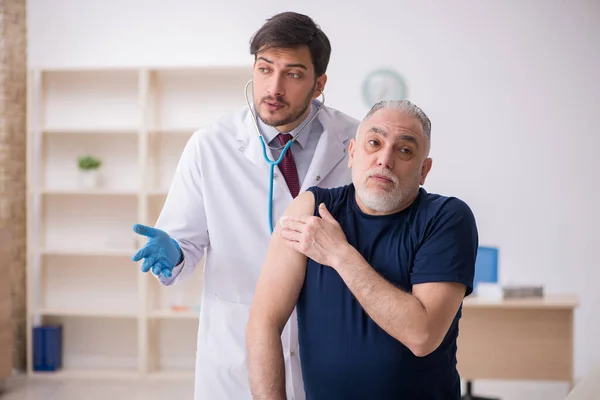 Yaşlı bir erkek hasta aşıyla genç bir doktoru ziyaret ediyor. — Stok fotoğraf