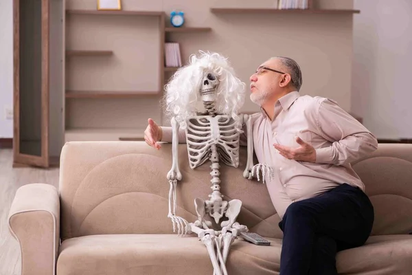 Vieil homme assis sur le canapé avec le squelette féminin — Photo