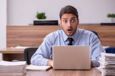 Genç bir erkek çalışan ve ofiste çok fazla iş var.