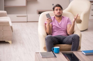 Genç adam salgın sırasında evde televizyon izliyor.