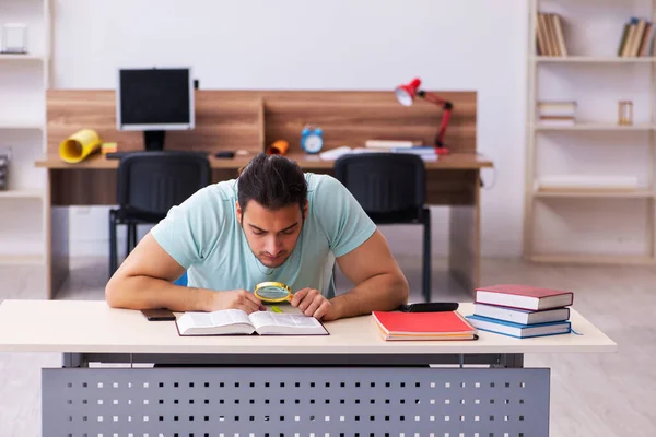 Joven estudiante masculino preparándose para los exámenes en casa sosteniendo la lupa — Foto de Stock