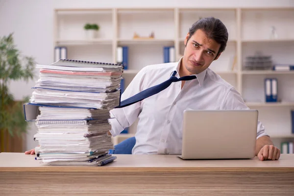 Ung manlig anställd och mycket arbete på kontoret — Stockfoto