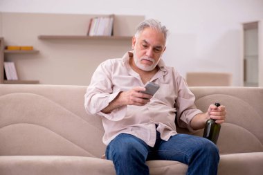 Yaşlı adam evde alkol içiyor.