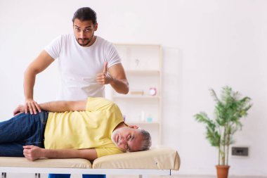 Yaşlı erkek hasta, genç erkek doktor masörünü ziyaret ediyor.