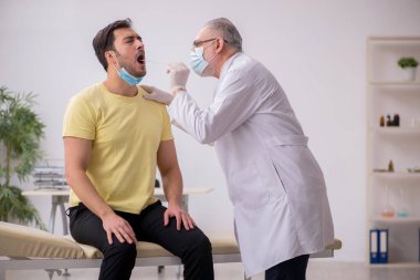 Genç erkek hasta yaşlı doktor otorhinolaryngologis 'i ziyaret ediyor.