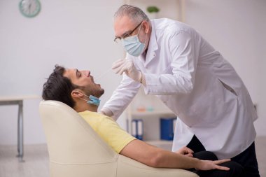 Genç erkek hasta yaşlı doktor otorhinolaryngologis 'i ziyaret ediyor.