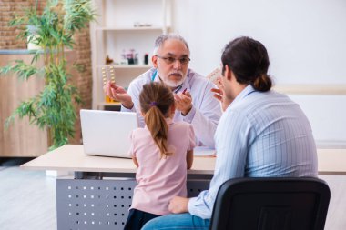 Babasıyla küçük bir kız yaşlı erkek doktoru ziyaret ediyor.