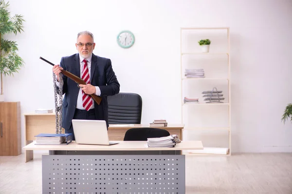 Un vieil homme d'affaires tenant un fusil dans son bureau — Photo