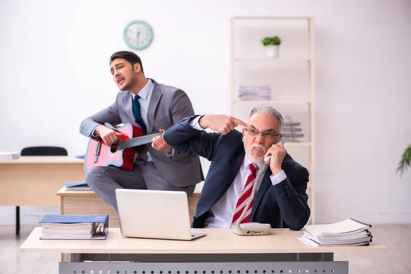 Young male employee playing guitar in the presence of old boss — Stock Photo, Image