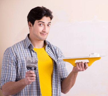 Evdeki duvara alçı yapıştıran genç adam.