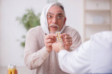 Yaşlı erkek hasta genç erkek doktor dişçiyi ziyaret ediyor.