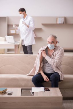 Genç erkek doktor aşı konseptinde yaşlı hastayı ziyaret ediyor.