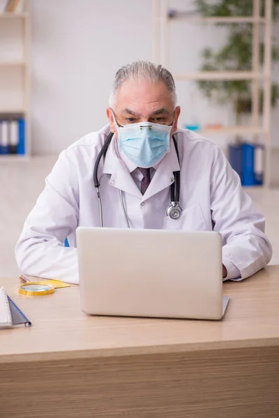 Yaşlı erkek doktor salgın sırasında klinikte çalışıyor. — Stok fotoğraf