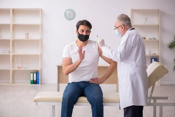 Jonge mannelijke patiënt op bezoek bij oude arts in vaccinatieconcept — Stockfoto