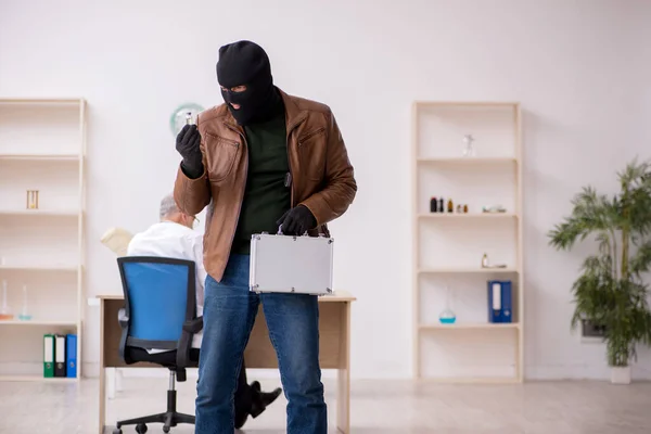 Masked man burglar stealing vaccine from old doctor — Stock Photo, Image