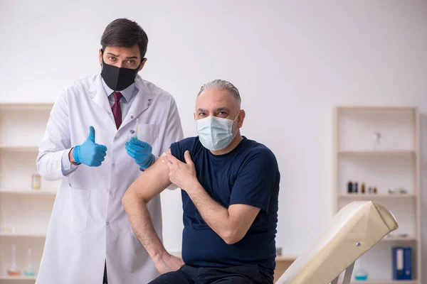 Oude mannelijke patiënt op bezoek bij jonge mannelijke arts in vaccinatiecentrum — Stockfoto