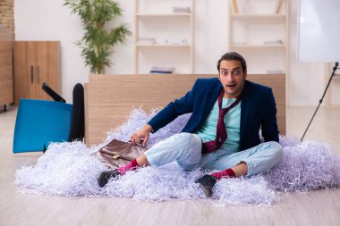 Genç bir erkek çalışan ve ofiste bir sürü kesik kağıt var.