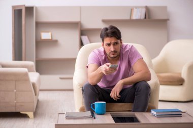 Genç adam salgın sırasında evde televizyon izliyor.