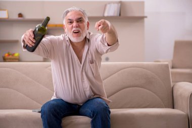 Yaşlı adam evde alkol içiyor.