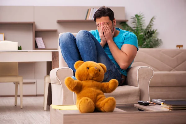 Jovem sentado com urso brinquedo em casa — Fotografia de Stock