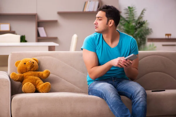 Молодой человек сидит дома с медвежьей игрушкой — стоковое фото