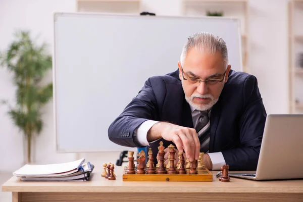 Viejo empleado jugando ajedrez en el lugar de trabajo — Foto de Stock