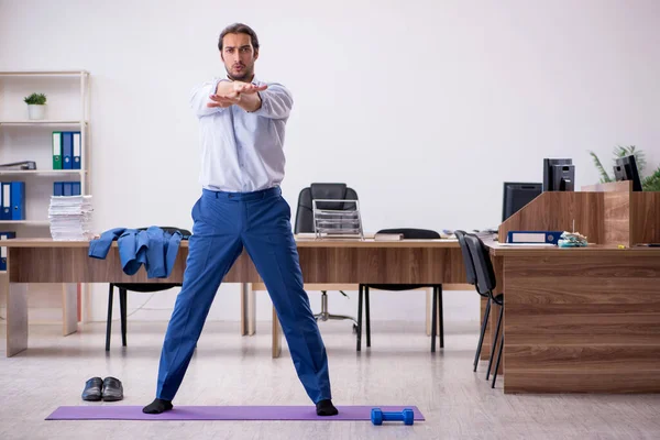 Jonge mannelijke werknemer doet sport oefeningen tijdens de pauze — Stockfoto