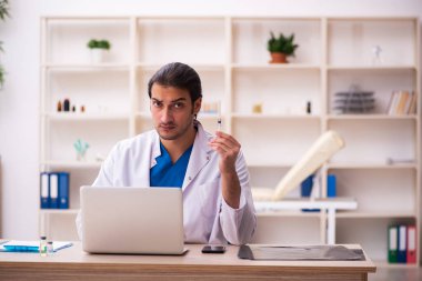 Genç erkek doktor klinikte şırınga tutuyor.