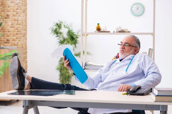 Old male doctor taking notes in the clinic — Stock Photo, Image