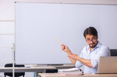 Genç erkek öğretmen beyaz tahtanın önünde.
