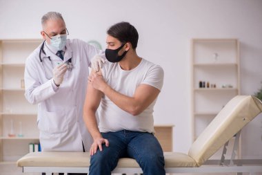 Genç erkek hasta aşı konseptinde yaşlı doktoru ziyaret ediyor.