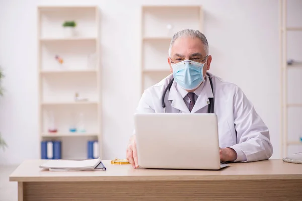 Yaşlı erkek doktor salgın sırasında klinikte çalışıyor. — Stok fotoğraf