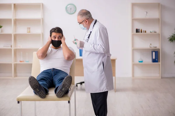 Genç erkek hasta aşı konseptinde yaşlı doktoru ziyaret ediyor. — Stok fotoğraf