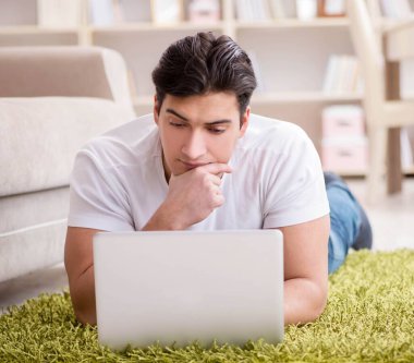 Evde, halı döşemesinde dizüstü bilgisayarda çalışan bir adam.