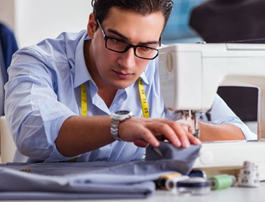 Genç terzi yeni elbiseler üzerinde çalışıyor.